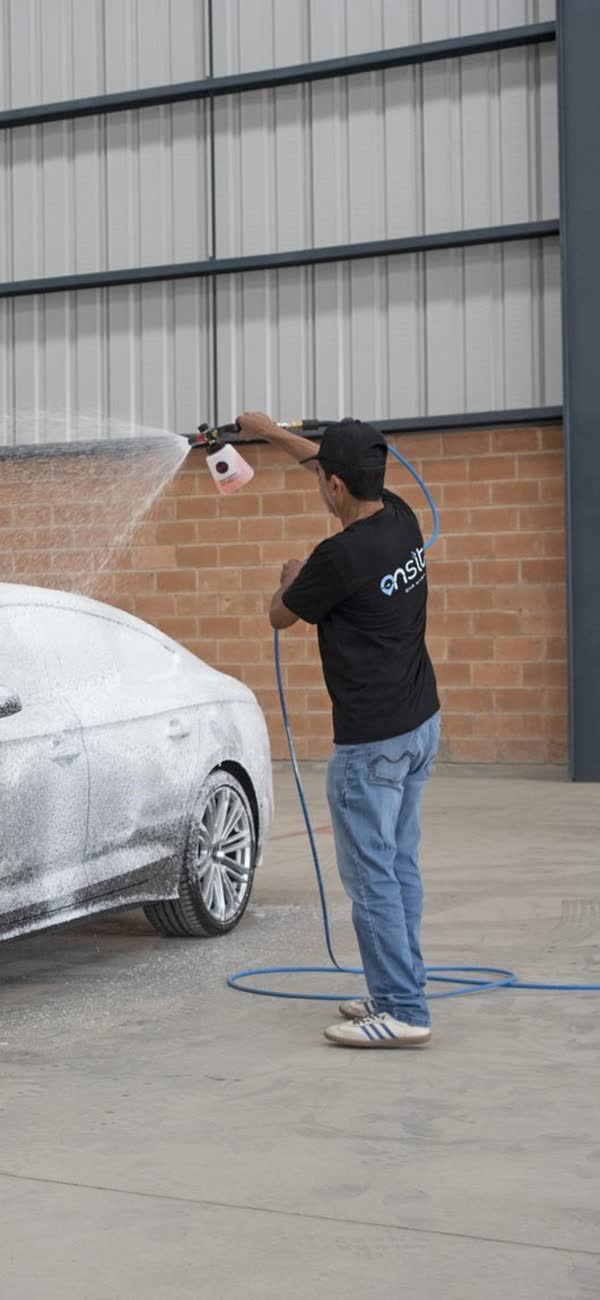 Un lavador de On Site llenando de espuma un auto en el estacionamiento